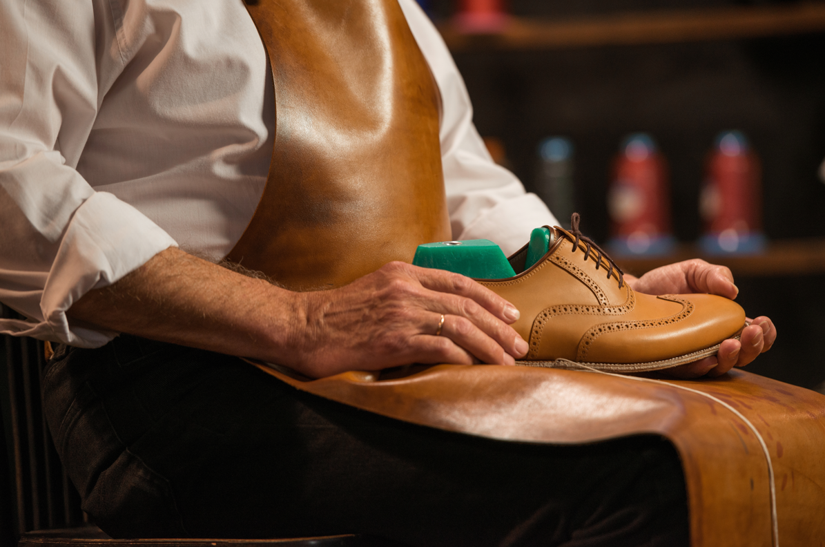 Main d'homme tenant une paire de Brogue et le déposant sur son tablier de cuir